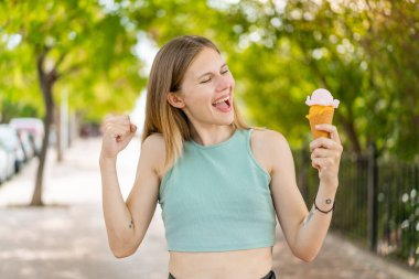 Açık havada kornet dondurmalı genç sarışın güzel kadın zaferi kutluyor.