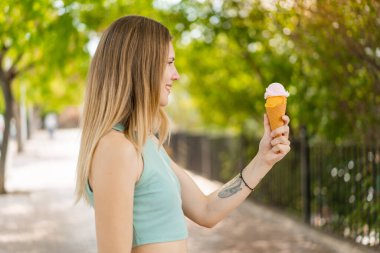 Genç, sarışın, güzel bir kadın. Açık havada kornet dondurması ve mutlu bir ifadesi var.
