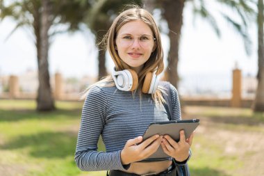 Açık havada elinde tabletle gezen genç sarışın kadın.
