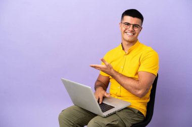 Genç adam dizüstü bilgisayarlı bir sandalyede oturmuş gülümserken bir fikir sunuyor.