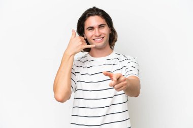 Beyaz arka planda izole edilmiş genç yakışıklı bir adam telefon hareketi yapıyor ve ön tarafı işaret ediyor.