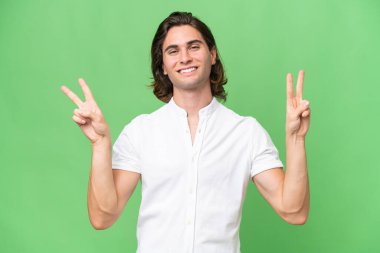 Yeşil krom arka planda izole edilmiş genç beyaz adam zafer işaretini iki elle gösteriyor.