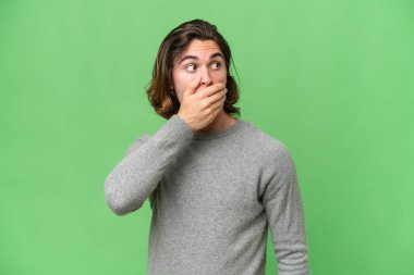 Genç beyaz adam yeşil krom arka planda izole edilmiş. Yan tarafa bakarken sürpriz jest yapıyor.