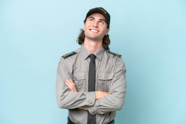 Genç güvenlik görevlisi mavi arka planda izole edilmiş gülümserken yukarı bakıyor