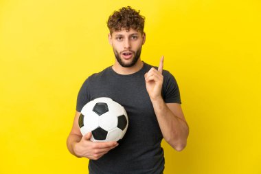 Yakışıklı genç futbolcu sarı arka planda izole edilmiş bir şekilde parmağını kaldırarak çözümü bulmaya çalışıyor.