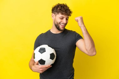 Yakışıklı genç futbolcu sarı arka planda izole edilmiş bir şekilde zaferi kutluyor.