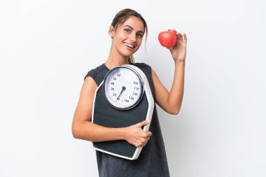 Genç, güzel Uruguaylı bir kadın beyaz arka planda, tartı makinesi ve elma ile izole edilmiş.