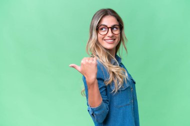 Genç Uruguaylı kadın, izole edilmiş arka planda bir ürünü sunmak için kenarı işaret ediyor.