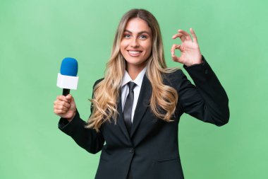 Genç, güzel Uruguaylı televizyon sunucusu izole edilmiş arkaplanda parmaklarıyla tamam işareti gösteriyor