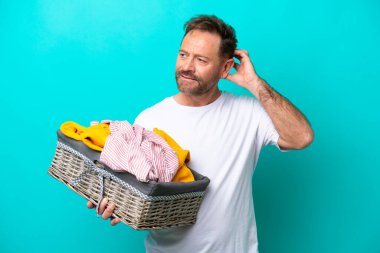 Mavi arka planda soyutlanmış çamaşır sepeti tutan orta yaşlı bir kadın şüpheleri var.