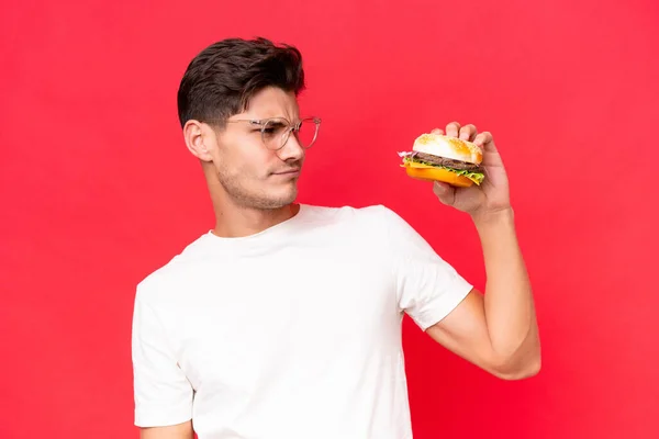 Jonge Blanke Man Met Een Hamburger Geïsoleerd Rode Achtergrond Met — Stockfoto