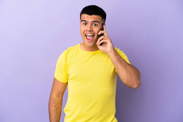 Молодой Красивый Мужчина Использует Мобильный Телефон Изолированном Фиолетовом Фоне Неожиданным — стоковое фото
