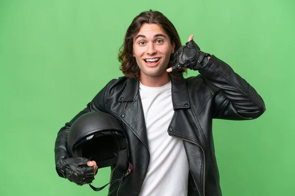 携帯電話のジェスチャーを作る緑のクロマの背景に隔離されたオートバイのヘルメットを持つ若いハンサムな男 サインを呼んでくれ — ストック写真