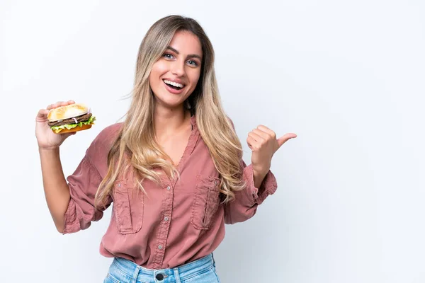 Młoda Ładna Urugwajska Kobieta Trzyma Hamburgera Odizolowanego Białym Tle Wskazując — Zdjęcie stockowe