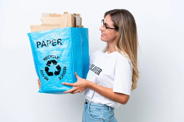 若いかなりウルグアイの女性は幸せな表情で白いクロマの背景に隔離されたリサイクルのための紙でいっぱいのリサイクルバッグを持っています — ストック写真