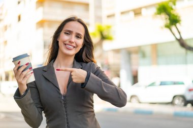 Genç bir kadın açık havada kahvesini alıp ona doğrultuyor.
