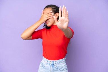 Mor arka planda izole edilmiş genç bir kadın dur hareketi yapıyor ve yüzünü kapatıyor.