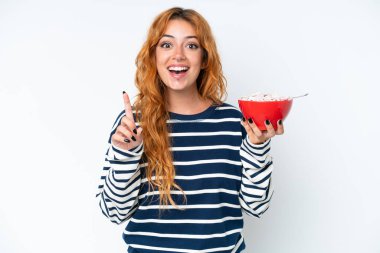 Beyaz arka planda kahvaltı sütü içen beyaz bir kadın harika bir fikre işaret ediyor.