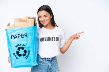 Young caucasian woman holding a recycling bag full of paper to recycle isolated on white background surprised and pointing finger to the side