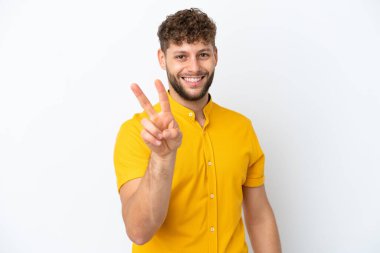 Beyaz arka planda izole edilmiş yakışıklı beyaz adam gülümsüyor ve zafer işareti gösteriyor.