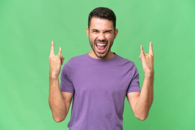 Genç, yakışıklı, beyaz bir adam izole edilmiş arka planda boynuz hareketi yapıyor.