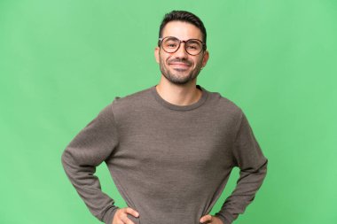 Soyutlanmış geçmişi olan yakışıklı beyaz bir adam. Kolları kalçasında ve gülümsüyor.