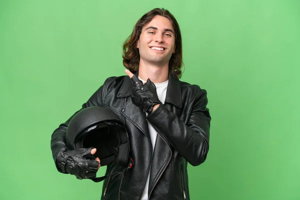 若いですハンサムな男とともにオートバイヘルメット隔離上の緑のクロマ背景を指す側に製品を提示します — ストック写真
