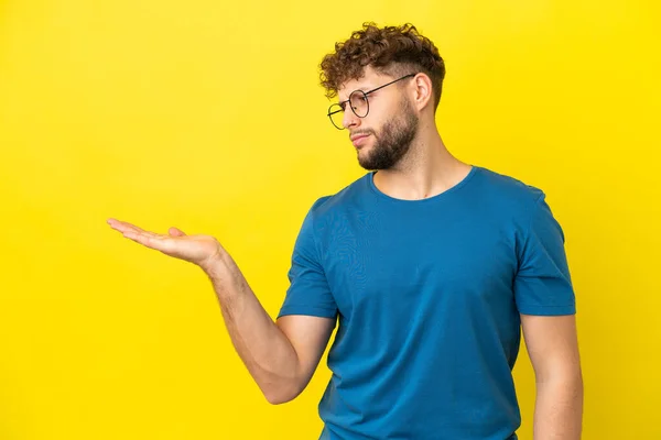 stock image Young handsome caucasian man isolated on yellow background holding copyspace with doubts