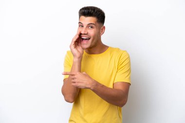 Beyaz arka planda izole edilmiş genç beyaz bir adam bir ürün sunmak ve bir şeyler fısıldamak için kenarı işaret ediyor.