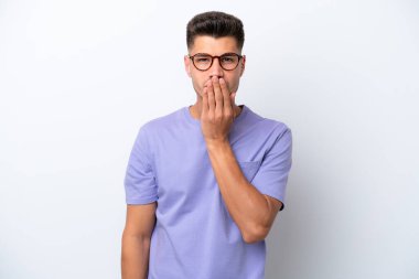 Beyaz arka planda izole edilmiş beyaz tenli genç bir adam ağızı eliyle kapatıyor.