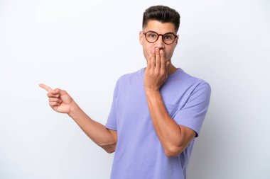 Beyaz arka planda izole edilmiş genç beyaz bir adam sürpriz bir ifadeyle işaret ederken...