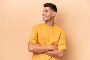 Young caucasian man isolated on beige background happy and smiling