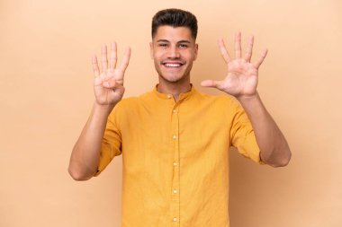 Beyazlı genç bir adam bej arka planda izole edilmiş dokuz parmaklı sayıyor.