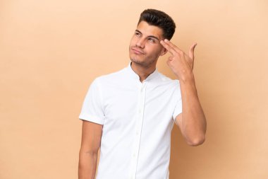 Genç beyaz adam bej arka planda izole edilmiş ve intihar jesti yapmada sorun yaşıyor.