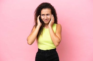 Pembe arka planda izole edilmiş genç İspanyol kadın hayal kırıklığına uğramış ve kulaklarını kapatmış.