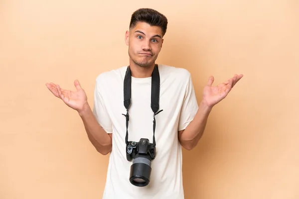 Jovem Fotógrafo Caucasiano Isolado Fundo Bege Tendo Dúvidas Levantar Mãos — Fotografia de Stock