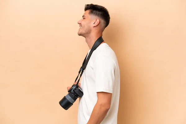 年轻的摄影师高加索人男子被隔离在米色背景的侧向位置上 — 图库照片