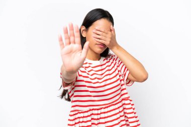 Beyaz arka planda izole edilmiş genç Kolombiyalı kadın jesti durdurup yüzünü kapatıyor.