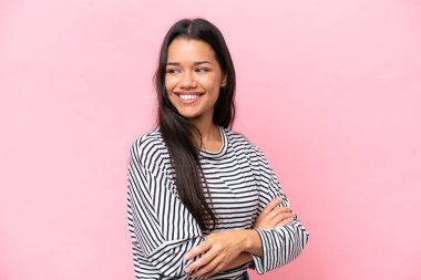 Pembe arka planda izole edilmiş, kolları bağlı ve mutlu genç Kolombiyalı bir kadın.