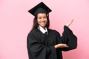 Üniversiteden mezun genç bir Kolombiyalı kadın pembe arka planda izole edilmiş ve davet edildiği için ellerini yana uzatıyor.