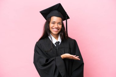 Üniversiteden mezun genç bir Kolombiyalı kadın pembe arka planda izole edilmiş bir şekilde bir fikir sunuyor.