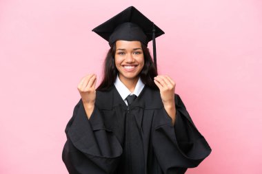 Kolombiyalı genç bir üniversite mezunu. Pembe arka planda izole edilmiş. Para hareketi yapıyor.