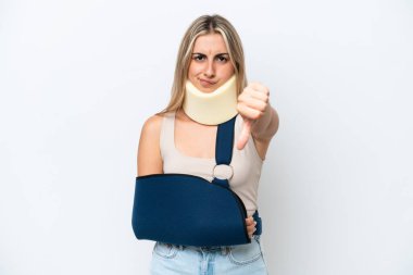 Woman with broken arm and wearing a sling isolated on white background showing thumb down with negative expression