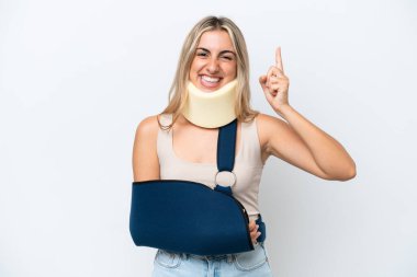 Kırık kollu ve askı takan bir kadın beyaz arka planda izole edilmiş ve en iyinin işareti olarak parmağını kaldırıyor.