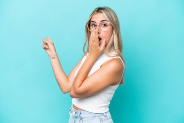 Mavi arka planda izole edilmiş beyaz bir kadın, sürpriz bir ifadeyle işaret ederken...
