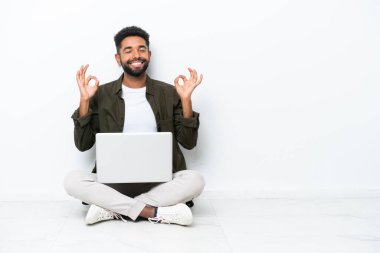 Yerde dizüstü bilgisayarı olan genç Brezilyalı bir adam Zen pozisyonunda beyaz tenli bir şekilde oturuyor.