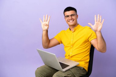 Dizüstü bilgisayarlı bir sandalyede oturan genç adam parmaklarıyla dokuz sayıyor.