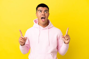 Genç yakışıklı, izole edilmiş sarı arka plan şaşırmış ve yukarı bakıyor.