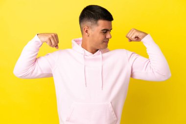 Soyutlanmış sarı arka planda genç yakışıklı adam güçlü bir jest yapıyor.