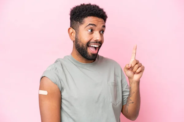 stock image Young Brazilian man wearing a band aid isolated on pink background intending to realizes the solution while lifting a finger up